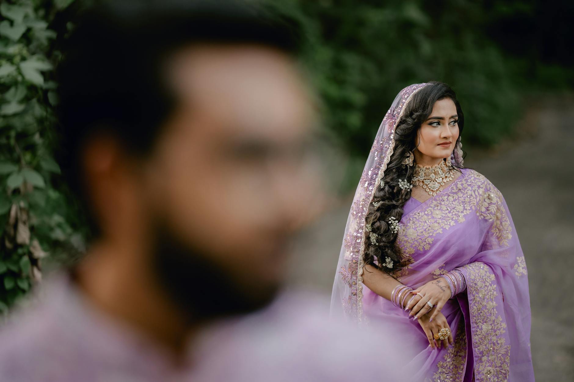 Panna młoda w fioletowym sari z biżuterią, mężczyzna rozmyty na pierwszym planie
